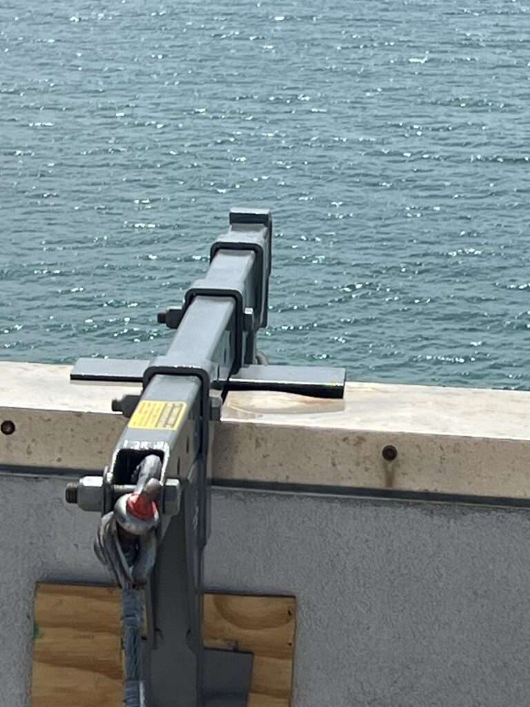 Metal beam extends over water with safety harness attached.