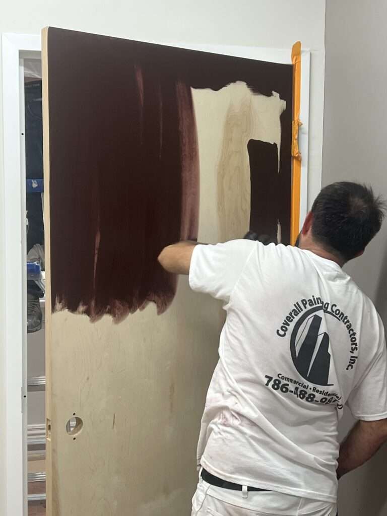 Painter applying brown paint to a wooden door.